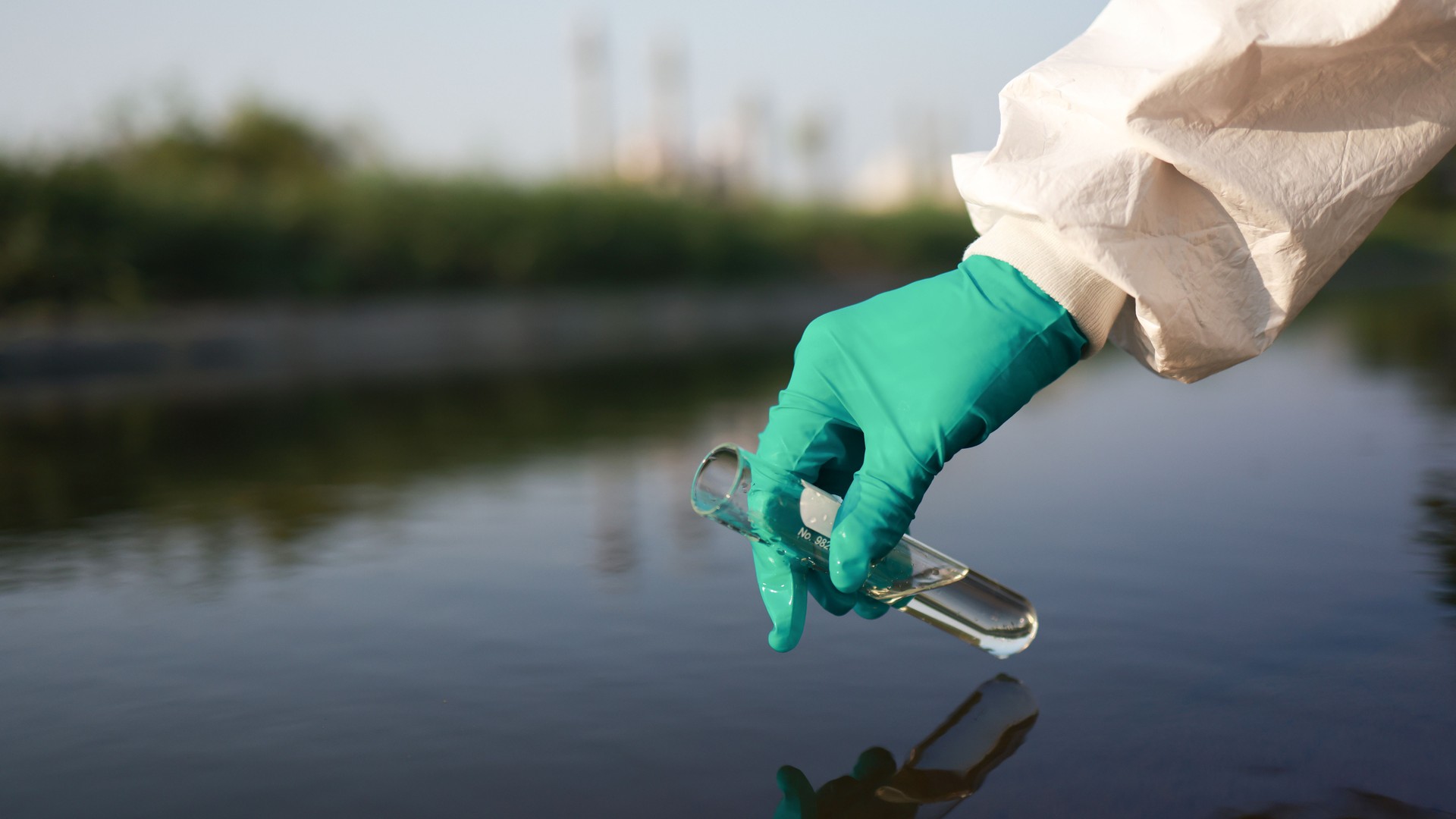 Close-up scientist or environment engineer's hand with a chemical protective suit and PPE collect a sample of toxic wastewater from a chemical flask  from an industrial